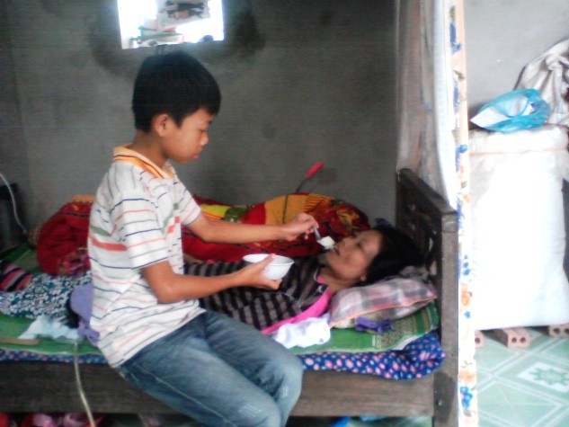 Cậu bé Đỗ Khắc Vinh đang bón cháo cho mẹ tại nhà.