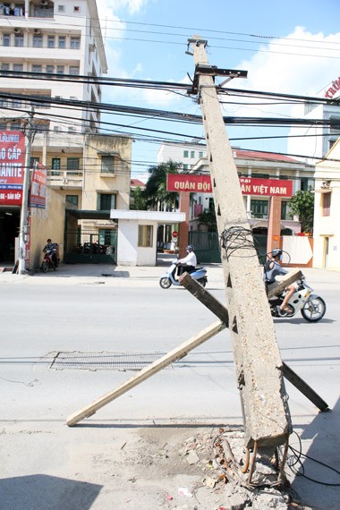 Thấy nguy hiểm, người dân gần đây đã dùng hai thanh gỗ để chống đỡ cột. Mớ dây cáp nặng trĩu như muồn kéo cột đổ xuống đường.