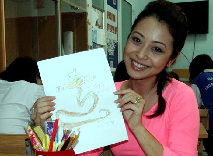 Hoa hậu cười rất tươi bên một bức vẽ có tên 'Thần rừng' với dòng chữ ký: Con tặng cô Jennnifer Phạm.