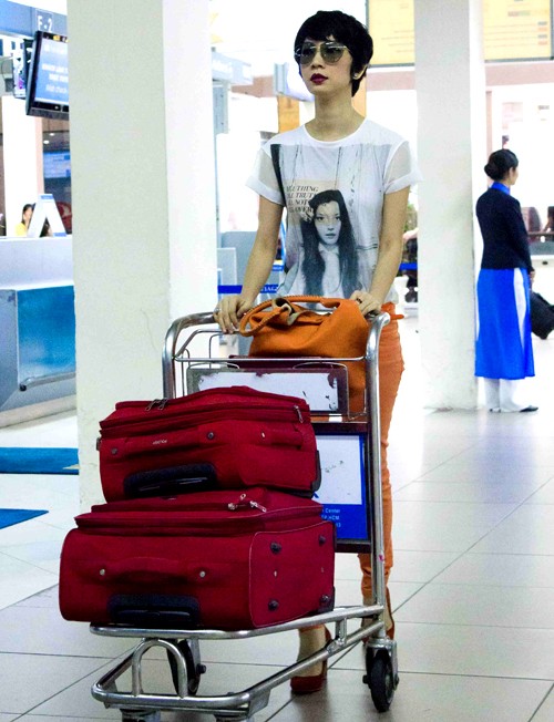Diện áo thun trắng, quần jeans cam và mang theo những chiếc valy hành lý màu đỏ, nữ giám khảo nổi bật tại sân bay.