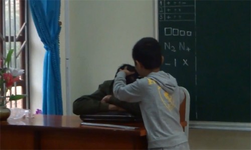 Cảnh thầy Nguyễn Như Tưởng, giáo viên dạy môn Thủ Công tại lớp 2A trong giờ học gục trên bàn được một nam sinh lên thoa dầu, nhổ tóc bạc (Ảnh cắt từ clip)