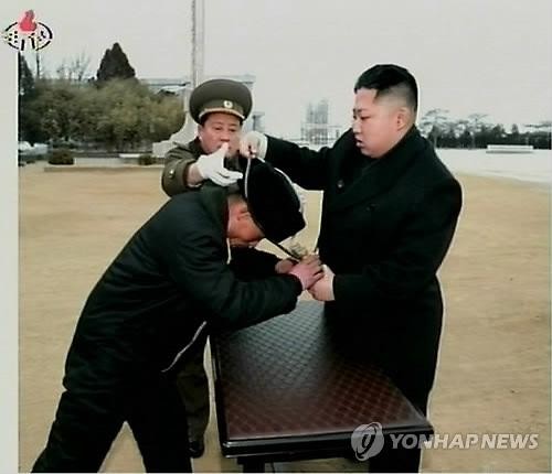 Lãnh đạo Triều Tiên Kim Jong-un (bên phải) đang treo một cặp ống nhòm qua cổ một quân nhân trong chuyến thăm một đơn vị hải quân. Ảnh được công bố bởi Đài truyền hình trung ương Triều Tiên ngày 7 tháng 2 năm 2012.