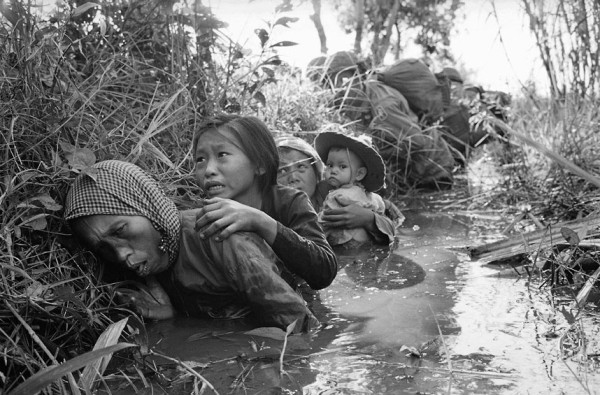 Bức ảnh này được chụp vào tháng 1 năm 1966. Người phụ nữ và những đứa trẻ núp mình trong một kênh bùn để tránh hỏa lực mạnh của du kích Việt tấn công lính Mỹ tại Bảo Trãi, khoảng 20 dặm về phía tây Sài Gòn.