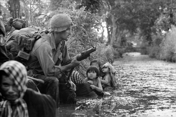 Hình ảnh này được nhiếp ảnh gia Horst Faas “chộp” lại vào tháng 1 năm 1966. Hai đứa trẻ Việt Nam nhìn chằm chằm vào một lính nhảy dù Mỹ đang nắm giữ một súng phóng lựu M79 khi chúng bám vào người mẹ đang cố gắng che chở cho con mình khỏi sự phản công của Việt Cộng trong khu vực Bảo Trãi, 20 dặm về phía tây Sài Gòn.