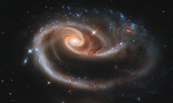 1. Bông hồng của Vũ trụ: Đây là hình ảnh dải thiên hà UGC 1810 hình đĩa dẹt bị dải thiên hà UGC 1813 phía dưới bóp méo do lực hấp dẫn, tạo thành một bông hồng tuyệt đẹp.Vệt lấp lánh màu xanh phía trên là sự kết hợp từ những chùm sao nhỏ màu xanh, điểm xuyết bằng những ngôi sao lớn đỏ pha ánh tím sáng chói .Đặc biệt là những cánh xoắn tạo thành từ phía bên phải của dải thiên hà UGC 1810, chúng có thể thay đổi các góc xoắn vì đang băng qua một dải thiên hà khác. Được biết, UGC 1810 là dải thiên hà nằm trong chòm sao Andromeda cách trái đất 300 triệu năm ánh sáng.