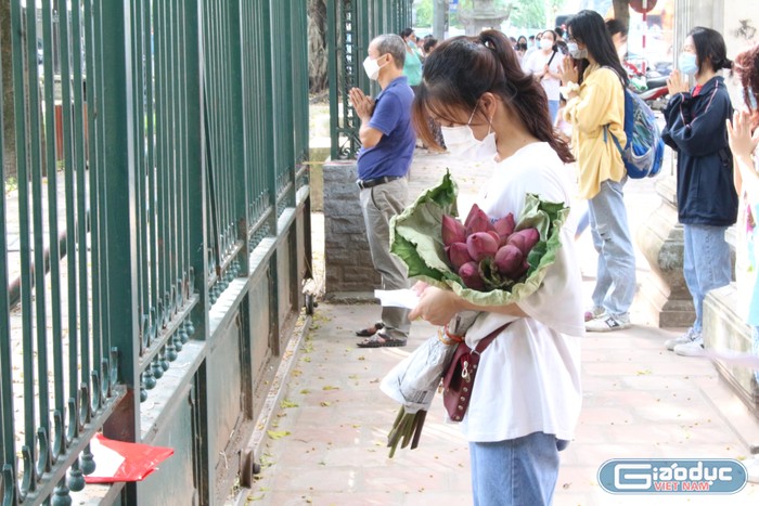 Một nữ sinh khác ôm bó hoa, trên tay cầm tờ giấy là &quot;công thức&quot; khấn, nghiêm túc cầu nguyện đứng trước cổng Văn Miếu Quốc Tử Giám.