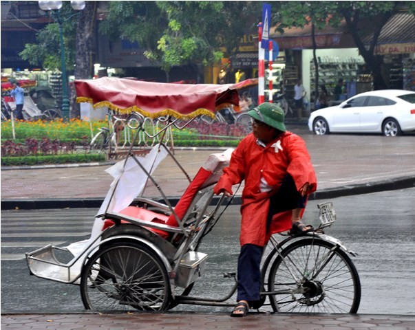 Người đàn ông làm nghề đạp xe xích lô vẫn ngồi trên phố với manh áo mưa để bắt khách.