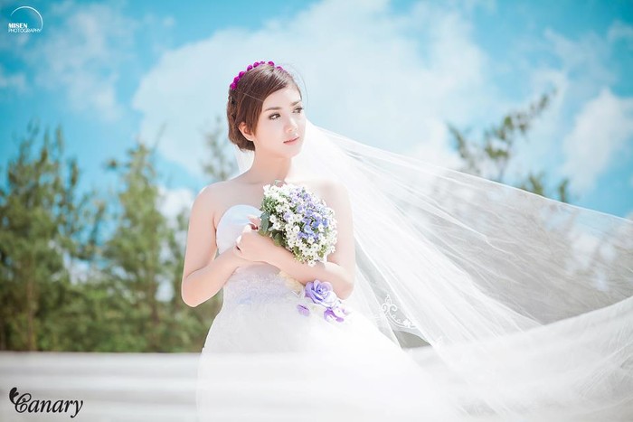 Thiên thần có gương mặt xinh xắn khiến diễn viên Hàn Quốc cũng phải ghen tỵ: Linh Napie tinh khôi trong màu áo cưới. Khăn voan đội đầu kết hợp với vòng hoa tự nhiên tuyệt xinh. Chiếc nơ hoa màu tím ở vòng eo là điểm nhấn nổi bật của chiếc váy cưới.