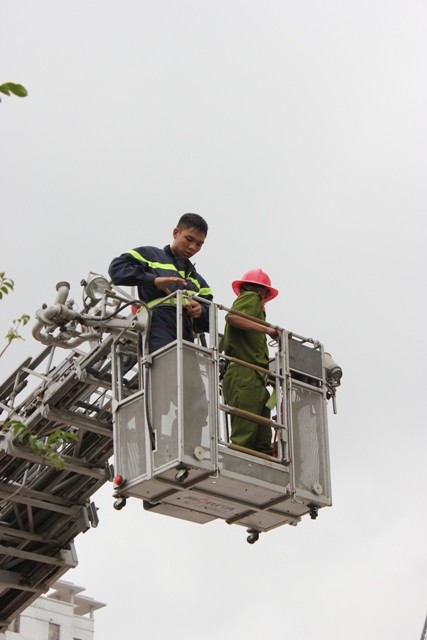 Lính cứu hỏa và đồng chí công an theo xe thang lên giải cứu người bị mắc kẹt phía trên tòa nhà.