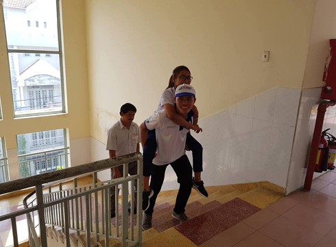 Thí sinh Y Nam được nam sinh viên tình nguyện cõng từ tầng trệt lên lầu 3 để đến phòng thi (ảnh: P.L)