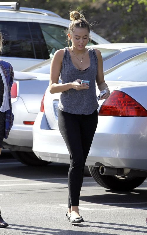 Miley Cyrus vừa đi bộ tay phải cầm chiếc điện thoại, còn tay trái cầm bao thuốc lá.