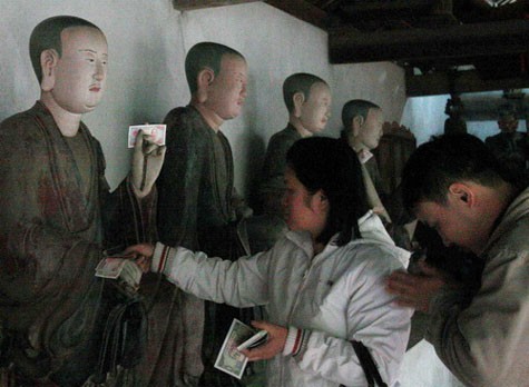 Tượng các vị La Hán chùa Tây Phương (Hà Nội) bị bội thực tiền rồi, nhưng cặp trai gái này vẫn cầm hàng ôm tiền lẻ, vừa vái vừa tìm cách nhét vào các kẽ có thể nhét trên “cơ thể” các tượng.