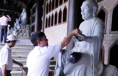 Đặt tiền lẻ lên tay tượng Phật ở chùa Bái Đính.