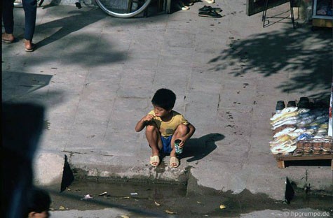 Một cậu bé ngồi đánh răng bên ven đường.
