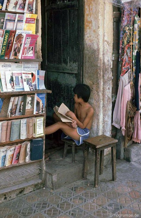 Hình ảnh một cậu bé vừa đọc sách vừa trông hàng giúp bố mẹ.
