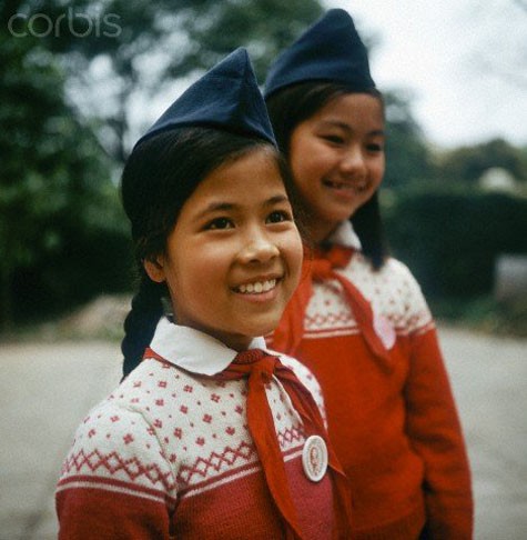 Hai cô bé học sinh Hà Nội đeo khăn quàng đỏ và đội mũ ca - lô trên đầu.
