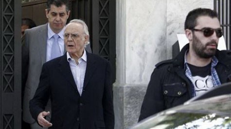Cựu bộ trưởng quốc phòng Akis Tsochadzopoulos (giữa) bị cảnh sát mặc thường phục giải đi từ nhà riêng ở Athens hôm 11-4 - Ảnh: AP