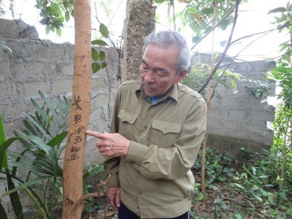 Ông Vân đang đứng bên cây nhãn nổi dòng chữ lạ trong vườn nhà mình