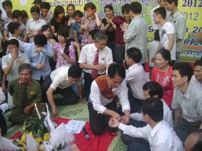 Những lưu học sinh Lào và Thái Lan đang cột chỉ chúc phúc cho các đại biểu khách mời và những người tham gia buổi lễ