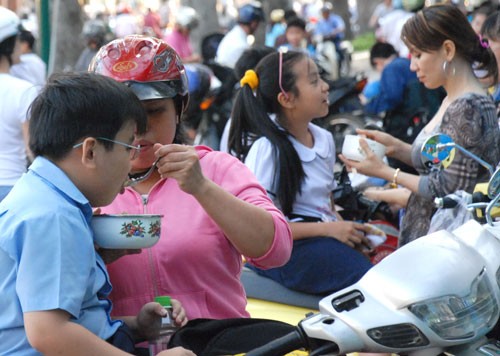 Cha mẹ tranh thủ cho con ăn ngoài đường cho kịp giờ học thêm ở TP.Hồ Chí Minh, ảnh trên báo Người Lao Động của tác giả Tấn Thạnh