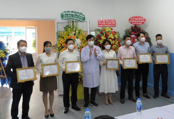 Tiến sĩ - Bác sĩ Lê Thanh Chiến - Giám đốc Bệnh viện điều trị COVID-19 Trưng Vương (thứ 4 từ trái sang) trao thư cảm ơn đến ông Ngô Minh Nhựt – Giám đốc Vietcombank Tân Định (thứ 3 từ trái sang) cùng các đơn vị đồng hành.