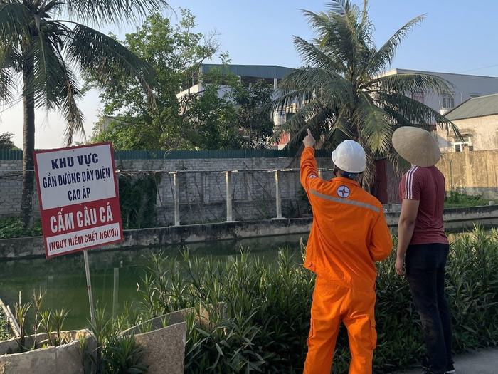 Công nhân Điện lực trực thuộc Công ty Điện lực Thanh Hóa cắm biển cảnh báo và tuyên truyền đến người dân không câu cá tại khu vực gần đường điện cao áp đi qua.