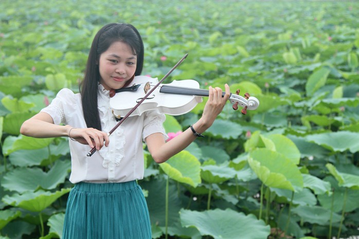 Thiếu nữ tạo dáng để chụp ảnh bằng cách chơi đàn bên hồ sen