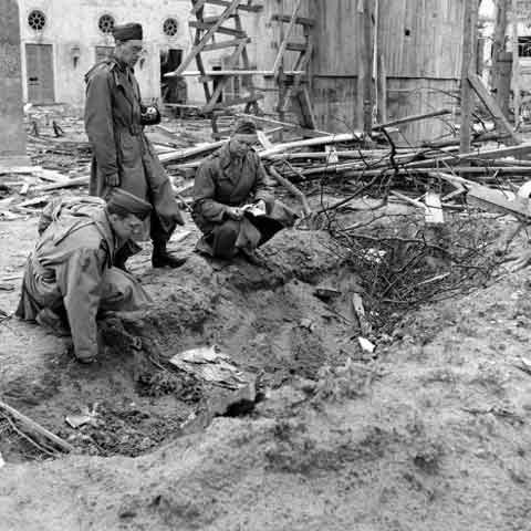 Ảnh chưa từng công bố: Phóng viên chiến tranh của LIFE là Percy Knauth (trái) nhìn qua đống rác thải ở một rãnh nướcq trong vườn của Thủ tướng Đức, nơi được cho là có xác của Hitler và Eva được chôn sau khi họ tự vẫn.