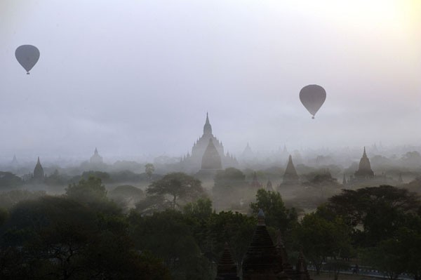 Những quả khinh khí cầu chở du khách bay lơ lửng trên bầu trời trong ánh bình minh, phía dưới là những ngôi chùa của thành phố cổ Bagan.