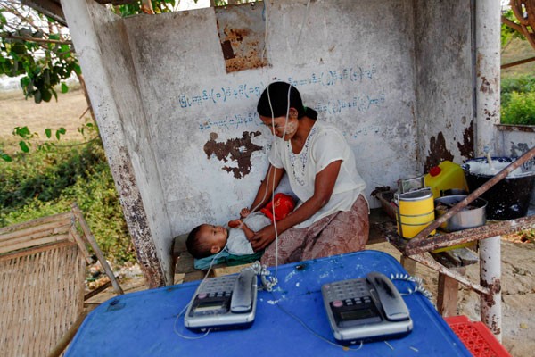 Người phụ nữ đang chơi đùa với đứa con của mình tại một trạm điện thoại công cộng thuộc thủ phủ Naypyitaw hôm 1/3/2012. Hiện tỷ lệ điện thoại và thuê bao Internet trên đầu dân của Myanmar đang ở mức thấp nhất khu vực.