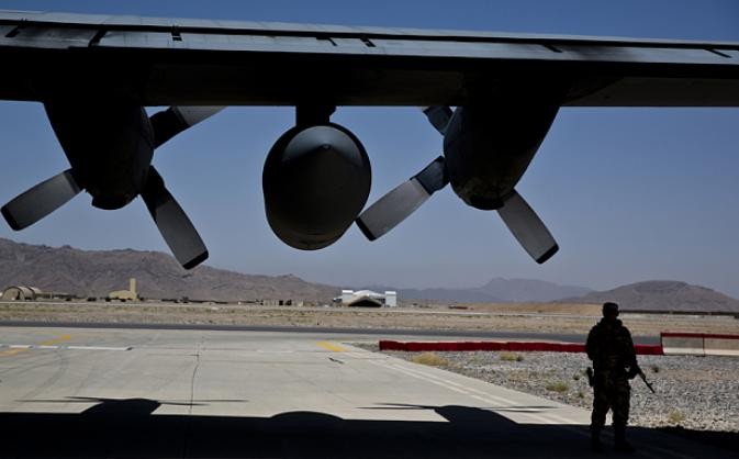 Một binh sĩ NATO đứng dưới cánh máy bay vận tải C-130 Hercules