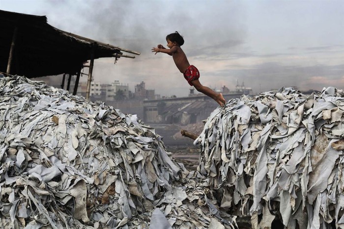 Một chú bé nhảy trên đống phế phẩm tại một xưởng thuộc da ở Dhaka, Bangladesh hôm 09/10. Những sản phẩm đồ da đắt tiền trên khắp thế giới được sản xuất trong khu xưởng tồi tàn này, nơi công nhân, trong đó có cả trẻ em phải chịu ảnh hưởng của các hóa chất độc hại và tai nạn nghề nghiệp. Nước thải độc hải từ các xưởng thuộc da này được xả thẳng xuống con sông chính của thành phố.