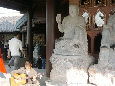 Người đàn ông mù lòa chơi bản đàn buồn bã và hát những lời ai oán về đời mình ngay cạnh những bức tượng La Hán (chụp tại chùa Bái Đính mới).