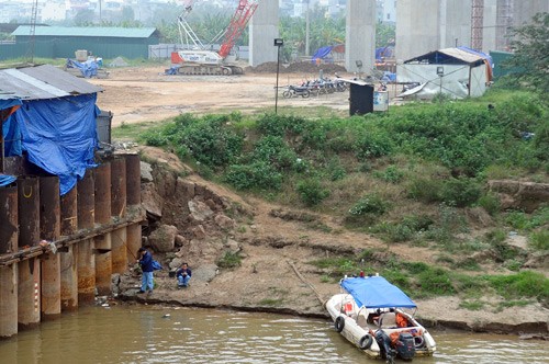 Dưới bờ sông, hai người đàn ông mặc đồng phục đang ngồi câu cá. Theo lời nhân viên bảo vệ, họ là những công nhân thi công tại đây.