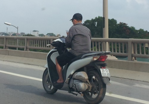 Chạy xe máy không đội mũ bảo hiểm, tay bấm điện thoại. Ảnh: Vu Kieu Hong Tu.