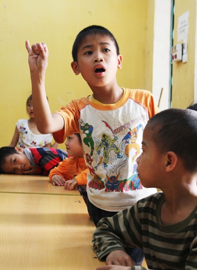 Cậu bé Thành đọc bảng chữ cái trong giờ tiếng Việt. Ở trường, các em nhỏ như Thành (từ 6 đến 16 tuổi) được giáo viên dạy đọc, viết, tính những phép tính đơn giản từ lớp 1 đến lớp 5. Đủ 16 tuổi trở lên, các em sẽ được học nghề.