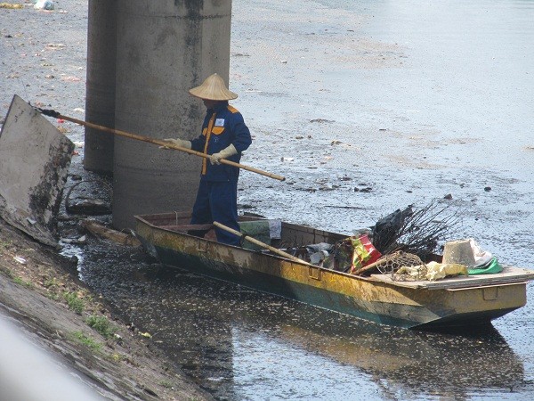 Công nhân vệ sinh môi trường đang cố gắng lấy những rác thải bị mắc làm tắc dòng chảy ở chân cầu.