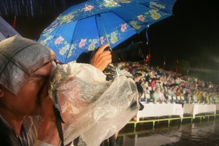 Mặc cho trời mưa, 1 phóng viên che khăn mùi xoa trên đầu và dùng bao ni lon để bảo vệ máy ảnh, tiếp tục tác nghiệp. Ảnh: Đại Dương/ Dân trí.