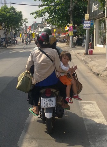 Xe máy hết chỗ ngồi, em bé phải ngồi trên đùi mẹ, quay ngược lại. Ảnh: Nguyễn Văn Tình.