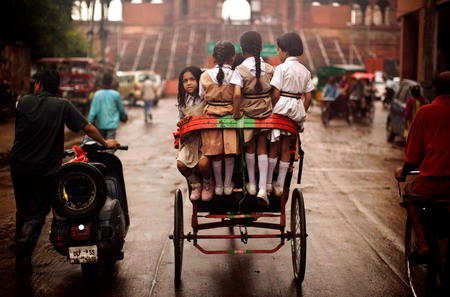 Các bé gái tiểu học Ấn Độ ngồi trên một chiếc xe lôi đúng lúc một cơn mưa rào ập đến ở gần đền Jama Masjid, New Delhi.