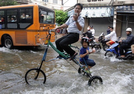 Hai bố con người Thái tỏ ra rất hứng thú trên chiếc xe đạp tự chế khi thủ đô Bangkok ngập nặng do nước sông Chao Phraya tràn bờ.