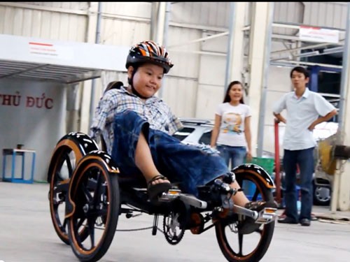 Bé Hùng phấn khởi thử ngồi trên chiếc xe đạp bẻ lái bằng vai dành riêng cho người khuyết tật tay.