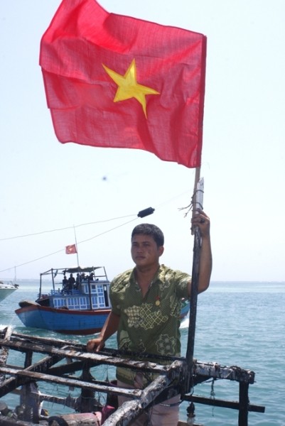 Anh Bùi Văn Phải bên lá cờ Tổ quốc cắm lại trên nóc tàu bị bắn cháy. Ảnh: Tiền Phong.