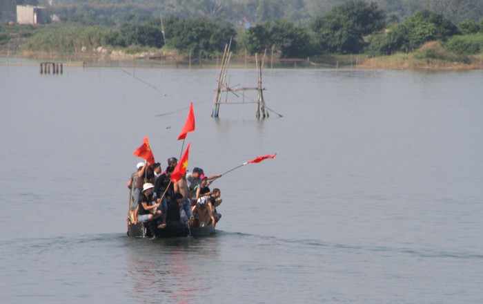 ...một nhóm cổ động viên chèo thuyền ra giữa sông, tay cầm cờ Tổ quốc reo hò cổ vũ nhiệt tình cho các đội đua.