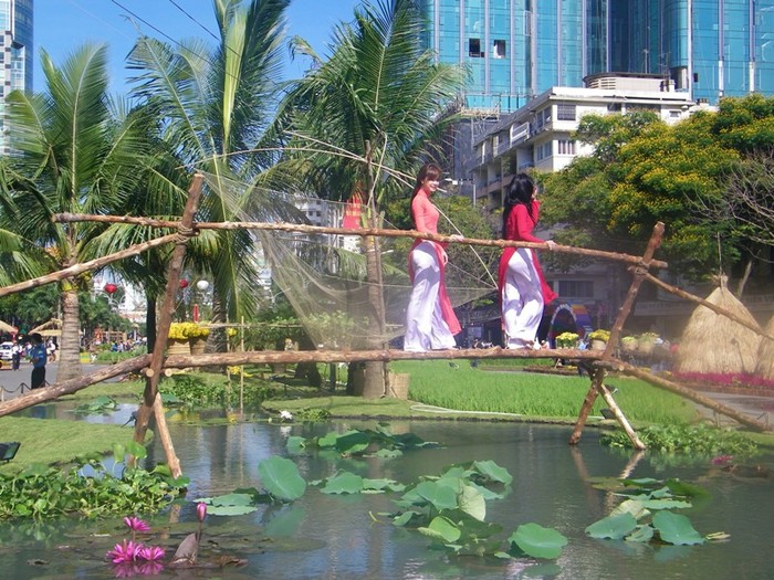 Khung cảnh lãng mạn nhất của đường hoa Nguyễn Huệ: Những cô gái quê đi trên chiếc cầu chênh vênh bắc ngang dòng sông hiền hoà, tái hiện một miền sông nước yên ả.