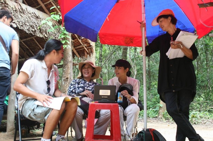 Việt Trinh (áo hồng, ngồi) trong vai trò đạo diễn, đang chỉ đạo diễn xuất phim Trở về.
