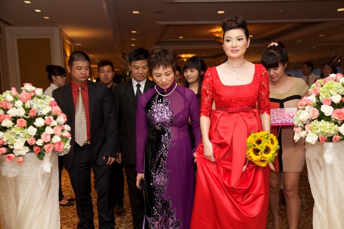 Và cô dâu Thuý Vinh trong tà áo dài cách điệu màu đỏ, tay cầm đoá hoa cúc vàng bước ra.