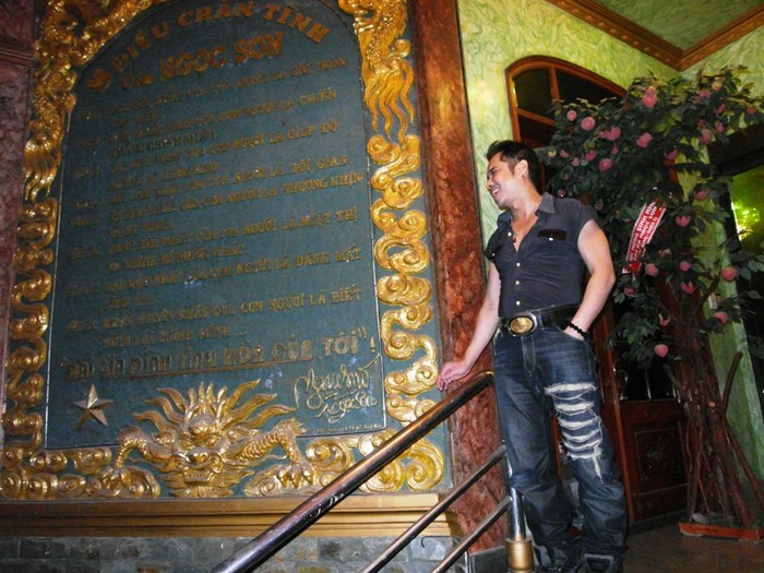 Ngọc Sơn đứng đón khách ngay cầu thang, bên cạnh "bảng vàng" những "lời vàng ngọc" mang tên "8 điều chân tình của Ngọc Sơn".