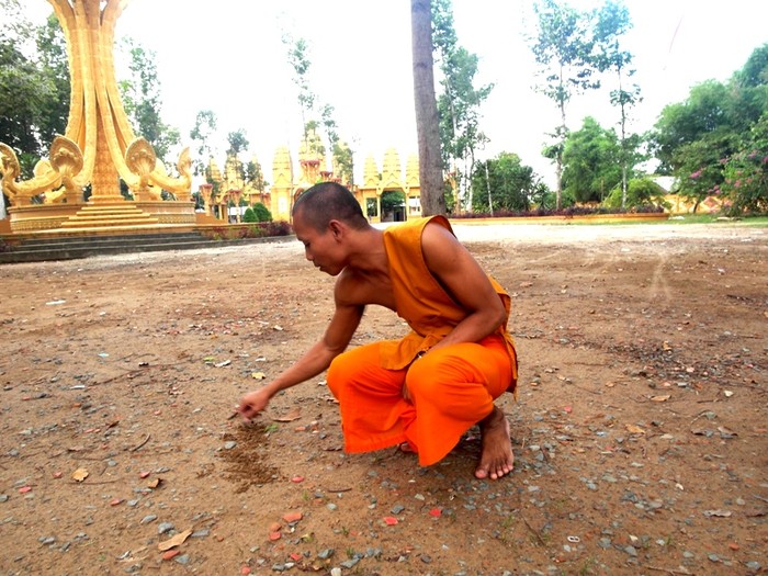 Vị sư trẻ người Khơme này đang viết trên nền đất bằng tiếng Việt tên ngôi chùa cho phóng viên xem.