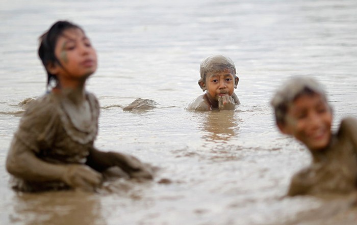 Trẻ em nông thôn chơi đùa trên sông, bùn đất đầy người